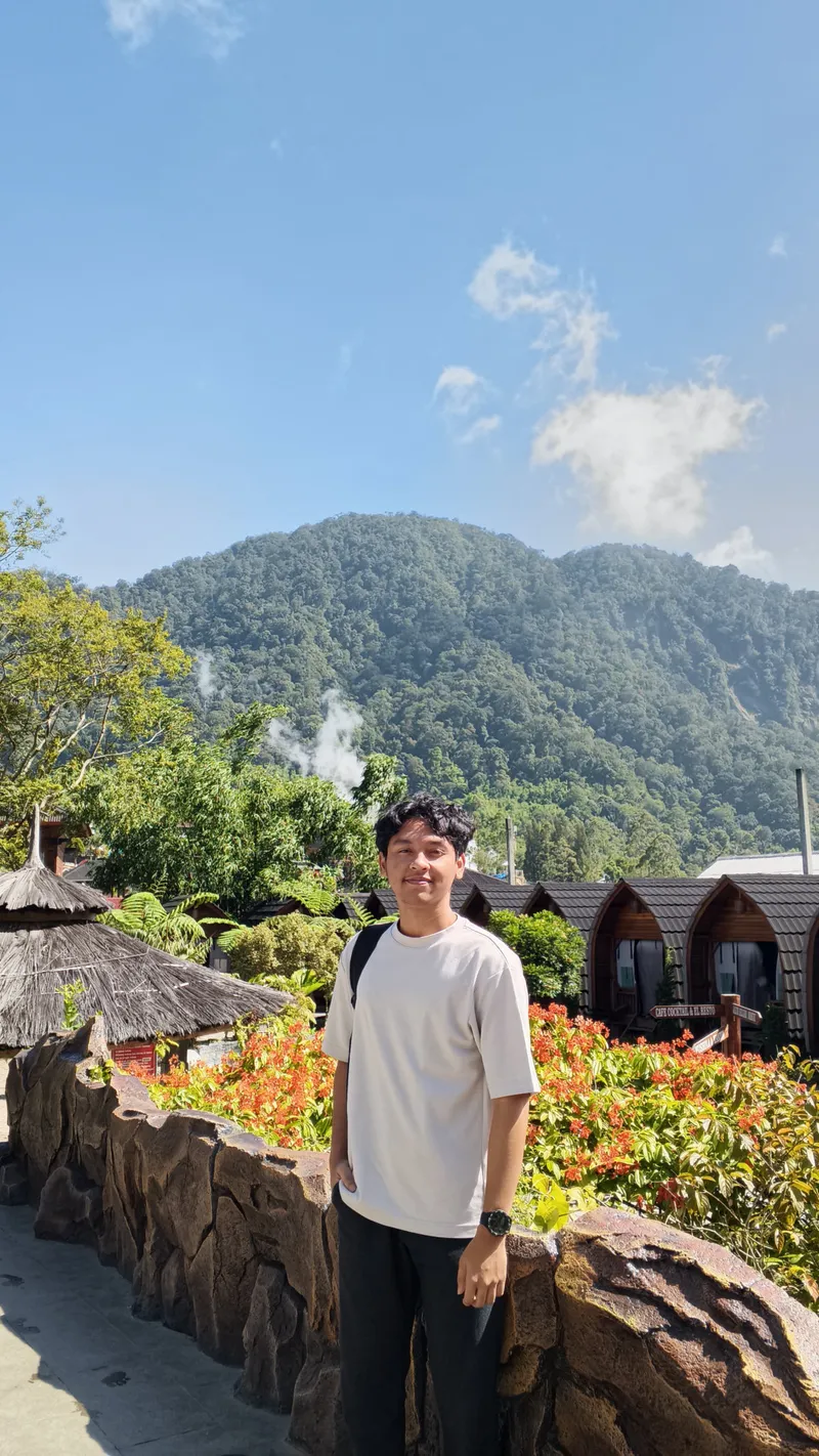 Joshua Palti Sinaga standing in a garden with mountains behind him